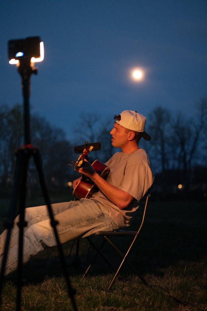 Conor Pederson playing acoustic guitar outdoors under the moon